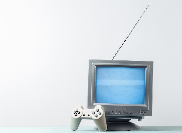Antenna old-fashioned retro tv receiver with gamepad on white wall.