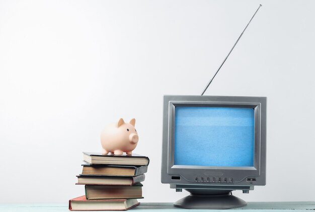 Antenne ouderwetse retro tv-ontvanger en stapel boeken met spaarvarken op witte muur