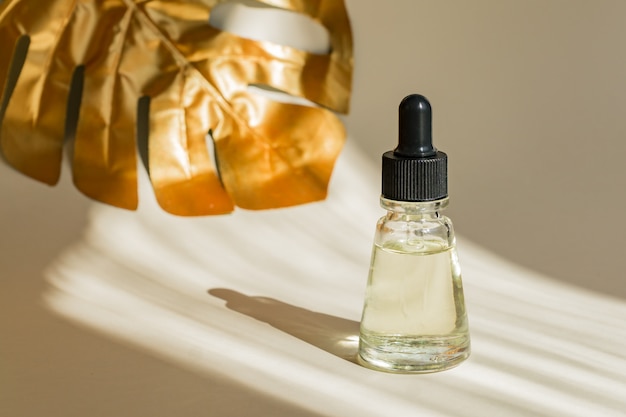 Anti-age serum met druppelpipet. Monstera gouden blad op de muur. Professionele fles voor gezichts- en lichaamsbehandeling