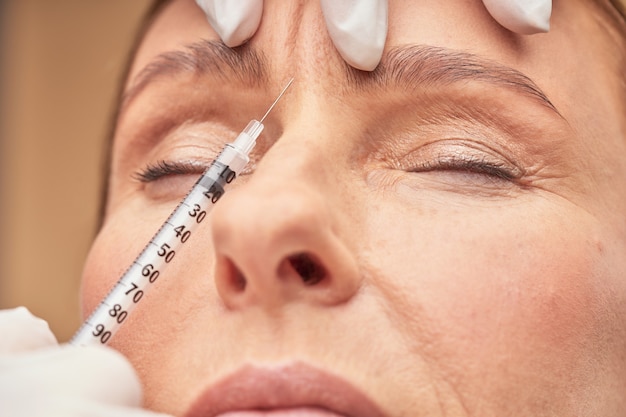 Foto procedure anti invecchiamento immagine ravvicinata dell'estetista in guanti protettivi che fa iniezione cosmetica in