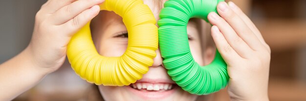 Anti-stress sensorische pop tube plastic speelgoed in kinderhanden. een kleine gelukkige kindjongen speelt thuis met een poptube-fidget-speeltje. kinderen houden en spelen pop buis gele en groene kleur. banier