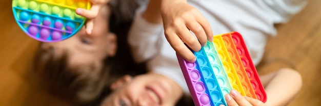 Giocattoli pop sensoriali antistress nelle mani di un bambino. un bambino felice gioca con un semplice giocattolo con fossette a casa. bambini piccoli che tengono e giocano a colori arcobaleno popit, tendenza 2021 anno. striscione