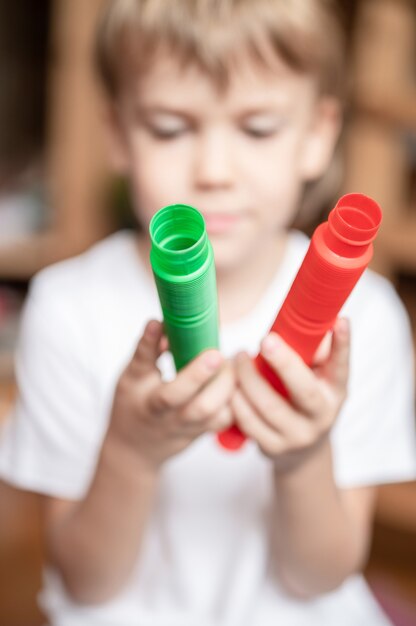 Anti stress sensory pop tube plastic toy in kid's hands. a little happy child boy plays with a poptube fidget toy at home. children holding and playing pop tube red and green color, trend 2021 year