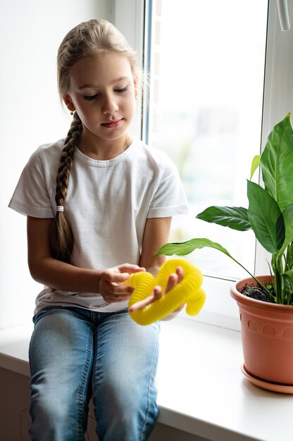 子供の手に抗ストレス感覚ポップチューブプラスチックのおもちゃ。小さな幸せな子供の女の子は家でpoptubeのそわそわおもちゃで遊んでいます。ポップチューブの黄色を保持し、遊んでいる子供たち、トレンド2021年