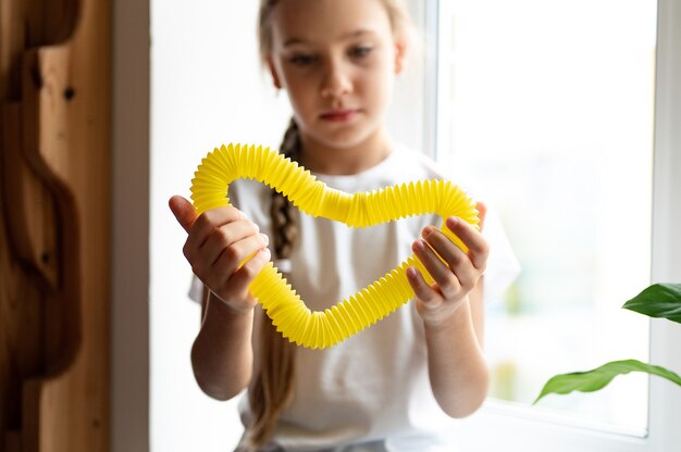 Anti stress sensory pop tube plastic toy in a kid's hands. a little happy child girl plays with a poptube fidget toy at home. children holding and playing pop tube yellow color, trend 2021 year