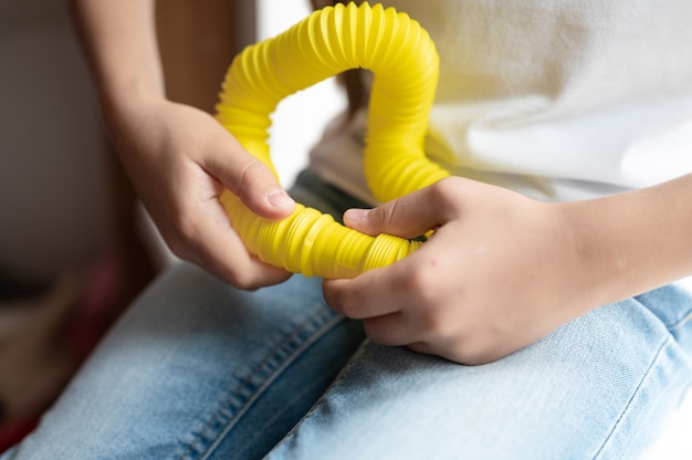 Giocattolo di plastica con tubo pop sensoriale anti stress nelle mani di un bambino. una bambina felice gioca con un giocattolo di fidget poptube a casa. bambini che tengono e giocano a tubo pop colore giallo, tendenza 2021 anno