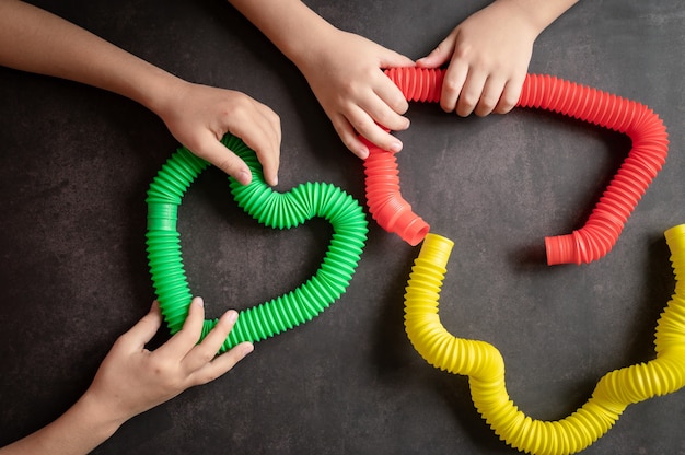 Giocattoli a tubo pop sensoriale anti stress nelle mani di un bambino. un bambino felice gioca con un giocattolo poptube su un tavolo nero. bambini piccoli che tengono e giocano tubi pop multicolore colore brillante, tendenza 2021 anno