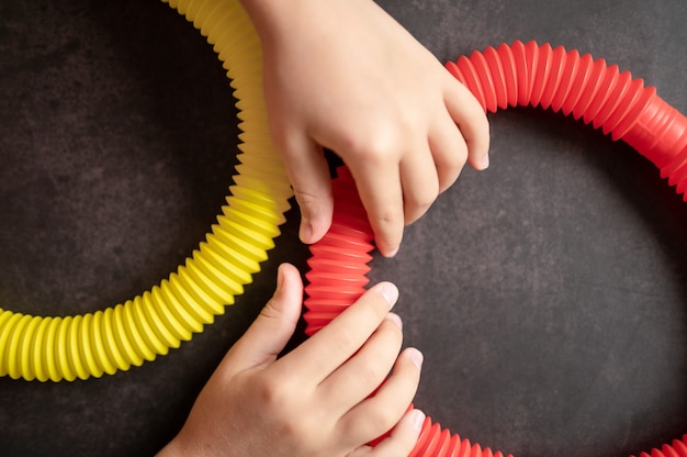 Anti stress sensory pop tube toys in children's hands. little happy kids plays with a poptube toy on a black table. toddlers holding and playing pop tubes red and yellow bright color, trend 2021 year