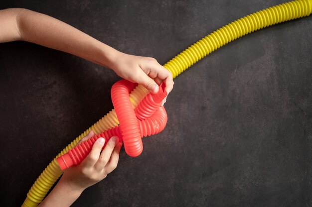 Anti stress sensory pop tube toys in children's hands. little happy kids plays with a poptube toy on a black table. toddlers holding and playing pop tubes red and yellow bright color, trend 2021 year