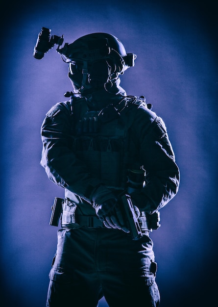 Anti terrorist squad fighter, army elite forces soldier in mask, with night vision device and tactical radio headset on helmet, armed service pistol standing ready for action, low key studio shoot