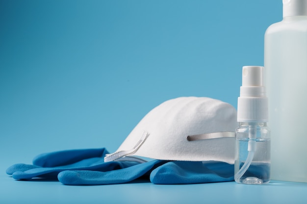 青色の背景、マスク、ゴム手袋、手の消毒剤ボトル、防腐剤ゲルのウイルス対策キット。
