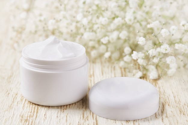 Photo anti wrinkle anti-aging  cream body care and face care hygiene moisture lotion with white flowers in plastic jar on wooden table.