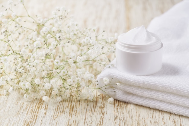 Crema antirughe antietà crema per la cura del corpo e cura del viso igiene idratante lozione con fiori bianchi in barattolo di plastica sul tavolo di legno.