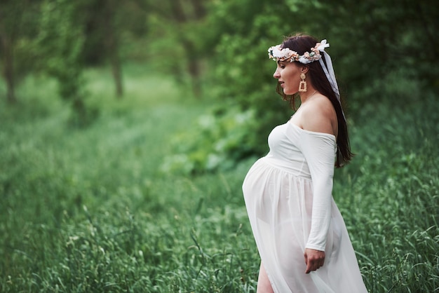 In anticipation. Beautiful pregnant woman in dress have a walk outdoors. Positive brunette