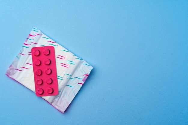 Anticonceptie pillen, hygiënische pads en tampons op blauwe achtergrond bovenaanzicht