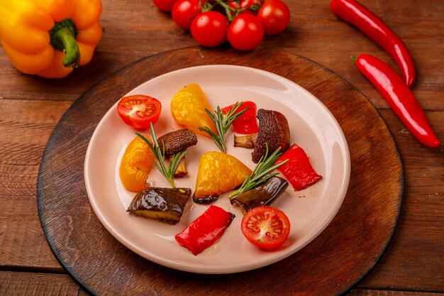 Antipasta on a plate on a stand on a wooden table next to fresh vegetables. Horizontal photo