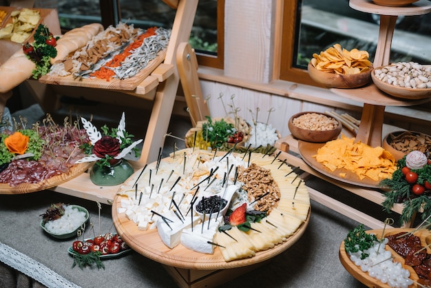 Antipasti board with various cheese and meat snacks with hummus\
and olives on wooden round board on black table