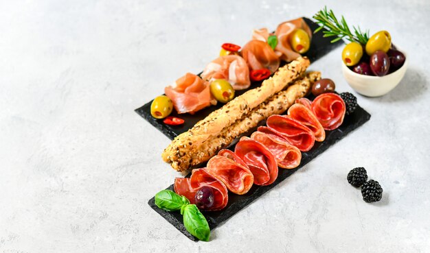 antipasti in italian restaurant with prosciutto and salami, olives, served on black stone dishes. 