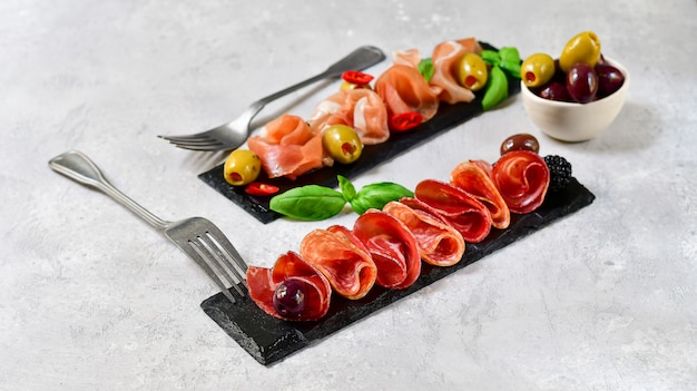 Photo antipasti in italian restaurant with prosciutto and salami, olives, served on black stone dishes.