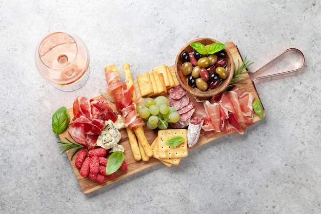 Tagliere per antipasti con prosciutto, salame, cracker, formaggio, noci, olive e vino rosato, vista dall'alto, piatto