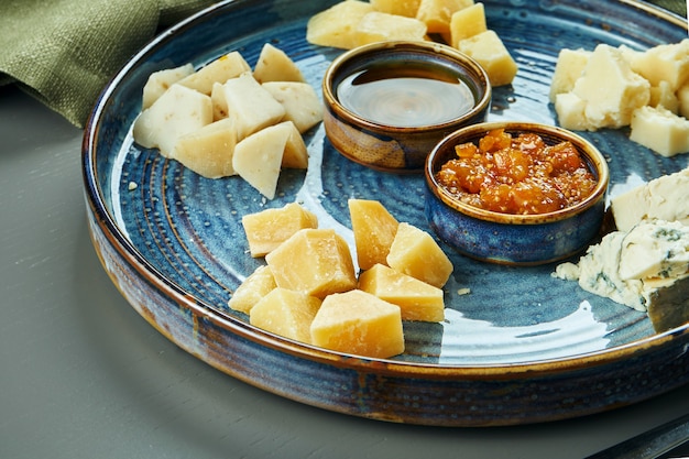 Foto antipasto - een kaasplateau. verschillende, zelfgemaakte kazen op een keramisch bord - brie, camembert, hollands met honing en noten. wijn voorgerecht. close-up, selectieve aandacht