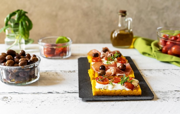 Antipasto met gegrilde polenta gegarneerd met stracchino kaas tomaten kruiden speck en olijf