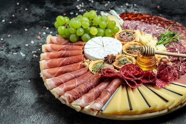 Antipasto platter cold meat plate with grissini bread sticks\
prosciutto slices ham grapes jamon ham beef jerky chorizo salami\
fuet pate and honey camembert goat cheese on wooden cutting\
board