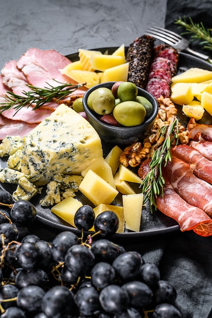 Antipasto platter with ham, prosciutto, salami, blue cheese, mozzarella and olives. Black background. Top view