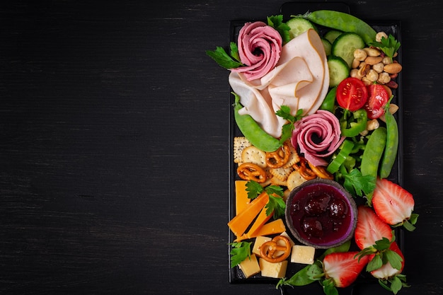 Antipasto schotel koud gesneden ham salami crackers aardbeien groenten en kaasschotel aan boord over donkere achtergrond voorgerechten tafel met italiaanse antipasti snacks bovenaanzicht