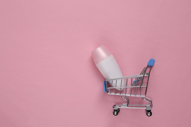 Antiperspirant roller in shopping trolley on pink background Top view