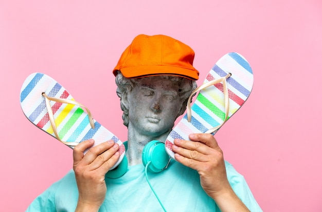 Antique bust of male in hat with headphones and flip-flops