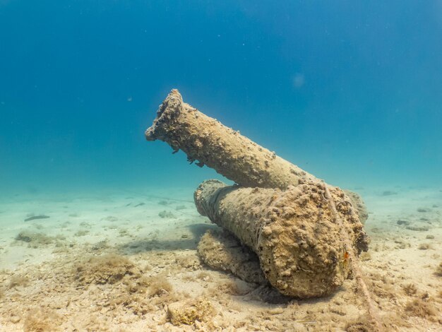 Antique cannons on a sandy sea floor turquoise water in the background