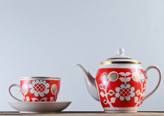 Antique ceramic cup and teapot on wooden table against a white wall