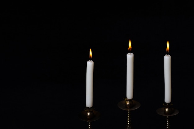 Antique copper candlestick with three burning white candles isolated on black background, copy space, close-up. Can be used as a design element