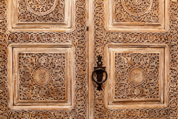 アンティークのドア。彫刻が施されたヴィンテージのスタイリッシュな木製のドア、大きなハンドルが付いた茶色。