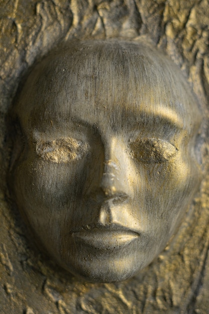 Photo antique face made of cement on the wall. the paint, cracked from time, is golden and white