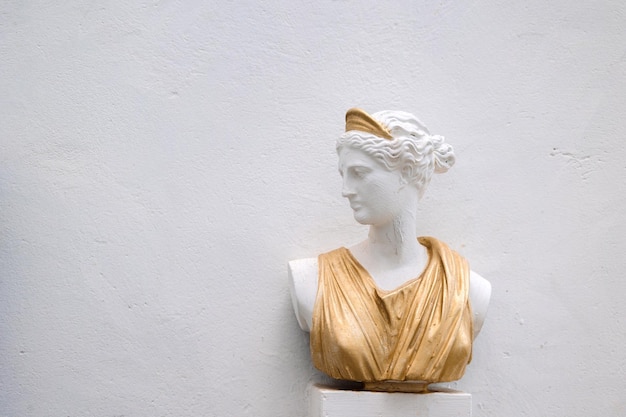 Antique head bust of woman against gray wall Historical statue in golden dress himation Ancient