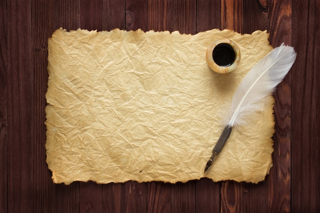 Antique paper, white quill and inkwell on wood