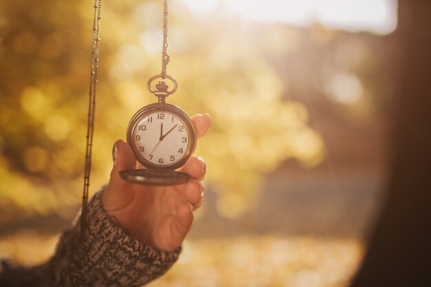 Photo antique pocket clock in hands on an autumn background