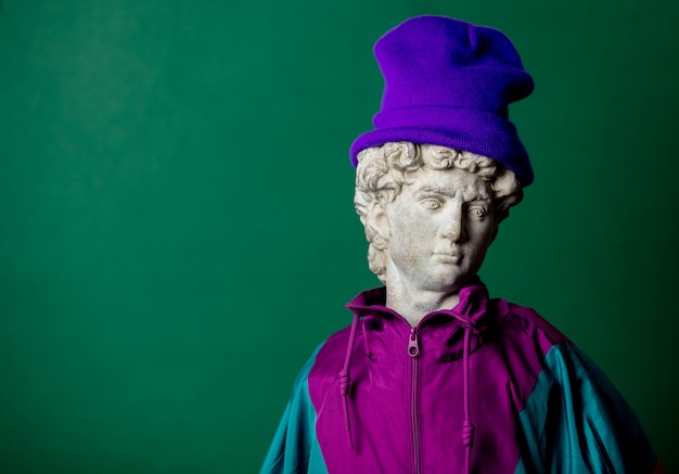 Antique statue dressed in trendy clothes of the nineties on green wall