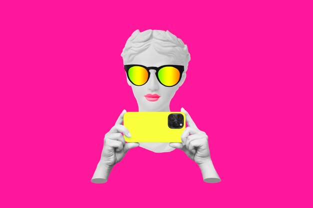 Antique statue head in sunglasses holding yellow mobile phone with photo camera in hand taking photo