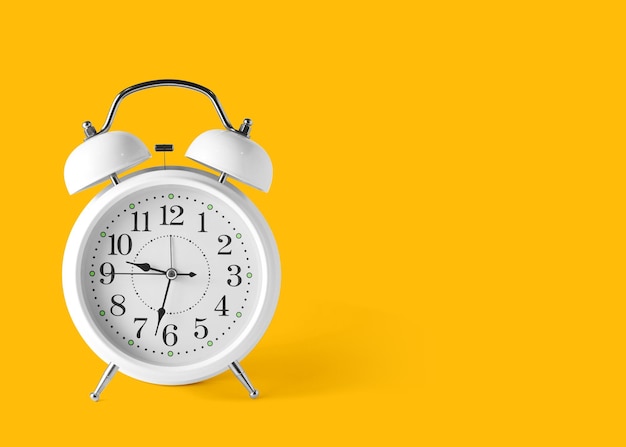 An antique white alarm clock on the floor with a bright yellow background in pastel colors