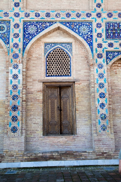 Antique wooden doors in a brick wall decorated with mosaics in the Gur Emir mausoleum in Samarkand, Uzbekistan. 29.04.2019