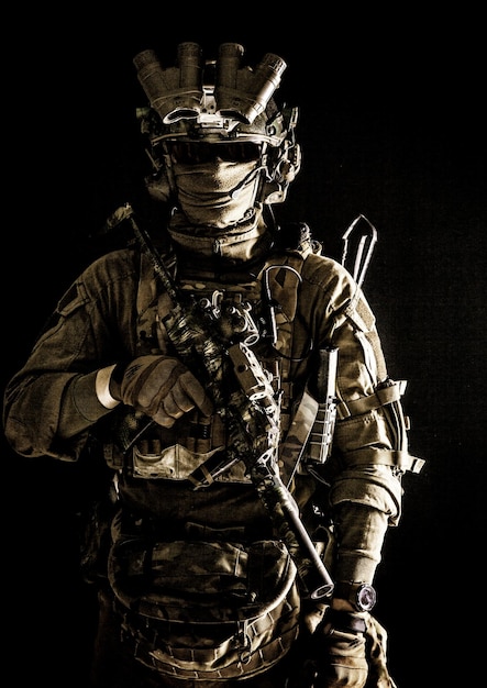 Antiterrorist squad fighter army elite forces soldier in combat uniform and tactical ammunition armed mini submachine gun wearing nightvision device low key studio portrait on black background