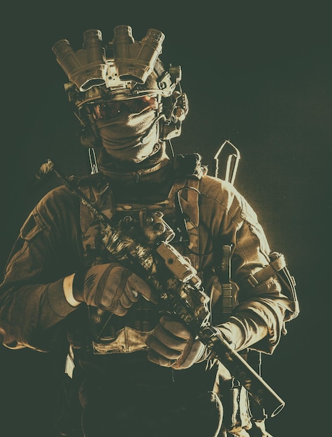 Antiterrorist squad fighter army elite forces soldier in combat uniform and tactical ammunition armed mini submachine gun wearing nightvision device low key studio portrait on black background