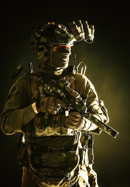 Antiterrorist squad fighter army elite forces soldier in combat uniform and tactical ammunition armed mini submachine gun wearing nightvision device low key studio portrait on black background