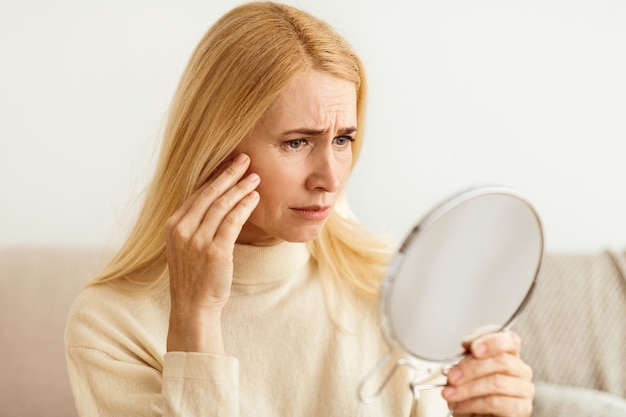 Antiwrinkle skin care sad woman looking in mirror touching her face