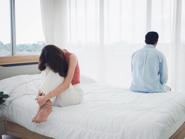 The anxiety of asian couple lovers on the bed sad young woman
and man sitting on the bed with relationship difficulties feeling
sad and thinking in the bedroom at home near the glass window