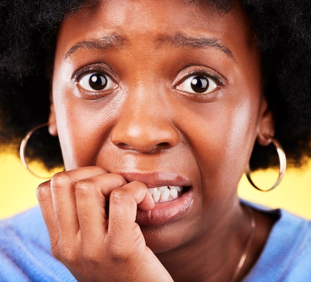 Anxiety biting nails and a woman scared in studio with fear mental health or nervous behaviour Face portrait of African person on yellow background worried stress or panic for phobia or horror