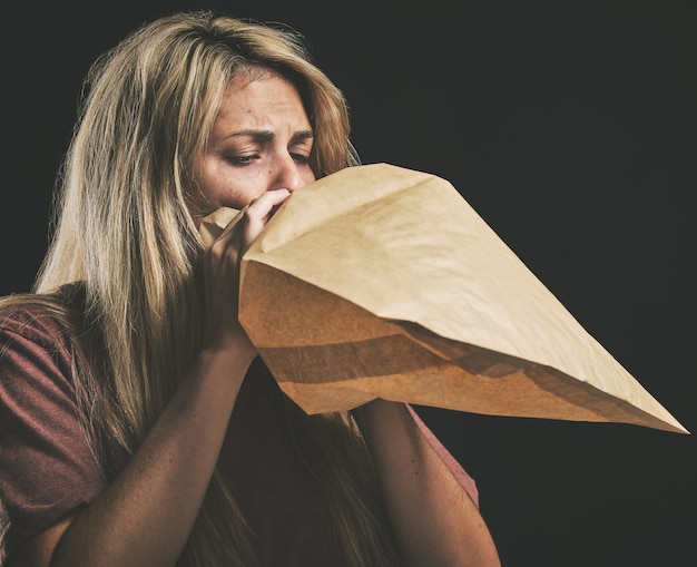 Anxiety breathing and scared woman with paper bag mental health and emergency oxygen air for lungs on black background Panic attack breathe problem stress and fear of depression nausea and sick